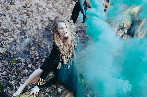 Shaman female holding hand green smoke bomb on  tree trunk
