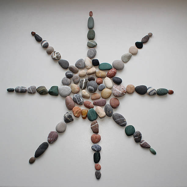 A symbol of the sun with rays, laid out from smooth sea pebbles on a white surface