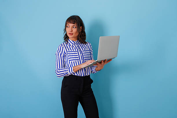 istock Young adult woman using a laptop, looking creatively to the side, representing ideas, technology, and professional work 2254037387