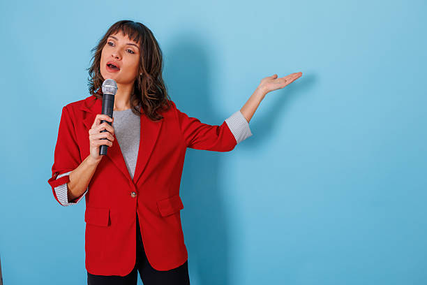 istock Woman in a red blazer actively speaking with a microphone, gesturing to an empty space for a message or product 2254038865