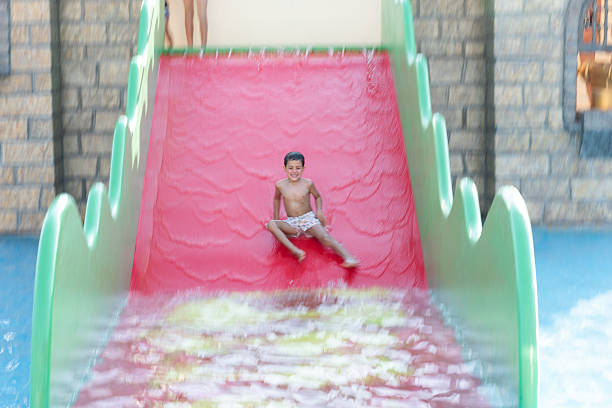 Child is enjoying summer vacation at a water park, laughing while sliding down a red and green castle-themed slide.