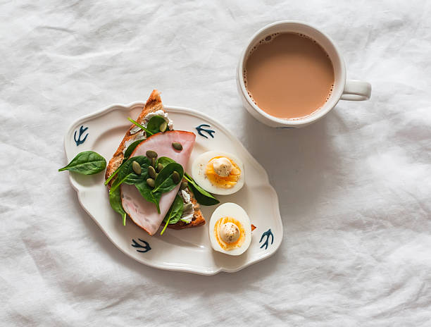 istock Delicious grilled breakfast - bread toast with cream cheese, spinach, ham, pumpkin seeds, boiled egg and coffee with milk on a light background, top view 2254039876