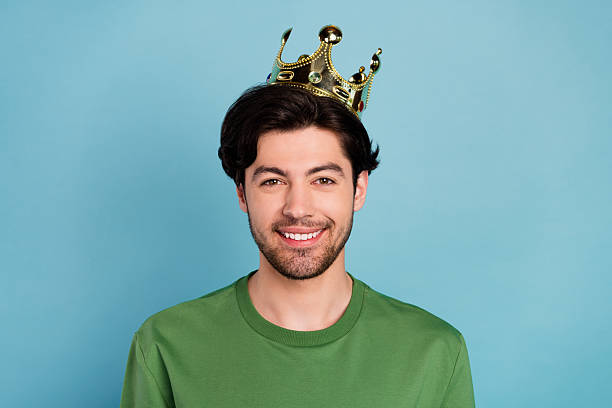 istock Portrait young handsome attractive nice looking smiling man wearing crown king isolated on blue color background 2254046756