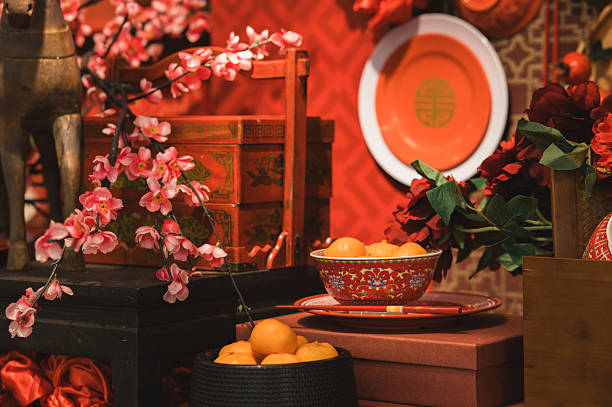 A festive Chinese New Year display with traditional red décor, cherry blossoms, and auspicious elements such as a decorative horse, red gift boxes, patterned plates, and mandarin oranges, symbolizing prosperity, good fortune, and celebration.