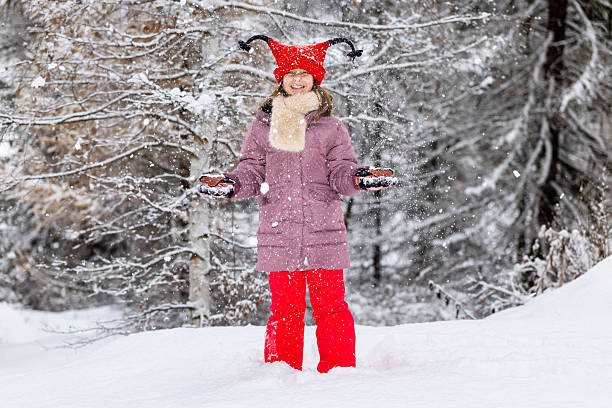 A cute little girl dressed in red stands out against the white winter landscape of the meadows and woods around Cogne, in the Aosta Valley. She is very happy about the snowfall on Christmas Day.