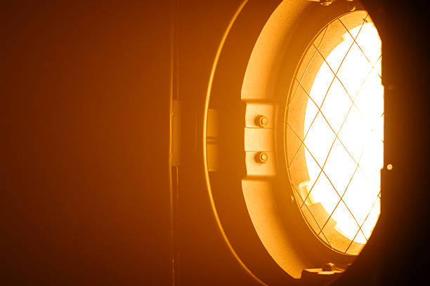 Close up of a powerful orange spotlight illuminating a dark room and creating a dramatic lighting effect. Lighting equipment backstage.