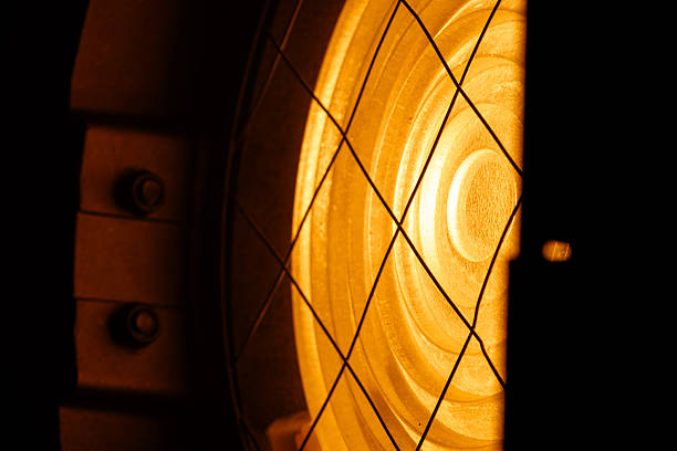 Close up of a glowing orange stage spotlight showing metal parts, bolts, and protective wire mesh. Lighting equipment backstage.
