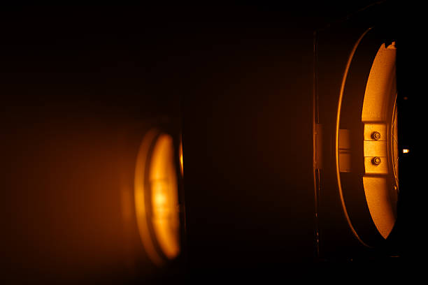 Two powerful studio spotlights emit warm orange beams in the darkness, creating a striking cinematic lighting effect. Lighting equipment backstage.