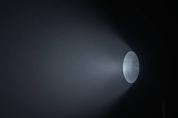 Close up of a modern spotlight emitting a cool white beam of light in a dark studio room with soft gradient shadows. Lighting equipment backstage.