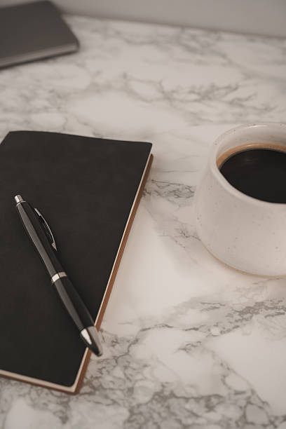 istock A black notebook and pen rest on a smooth marble table beside a white coffee cup filled with dark coffee. This scene captures a peaceful moment for creativity 2254070135