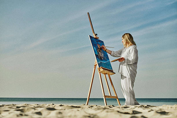 istock Young female artist painting on tranquil beach setting 2254071888