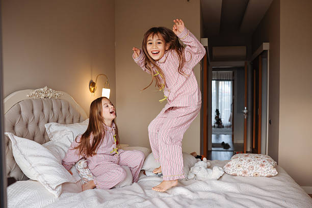 istock Two young sisters are jumping on a bed, having fun and enjoying their time together. 2254076142