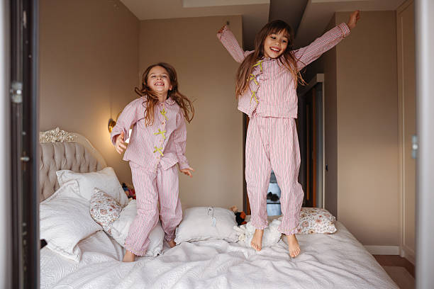 istock Two young sisters are jumping on a bed, having fun and enjoying their time together. 2254076940