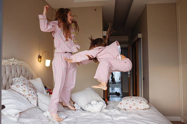 istock Two young sisters are jumping on a bed, having fun and enjoying their time together. 2254077111
