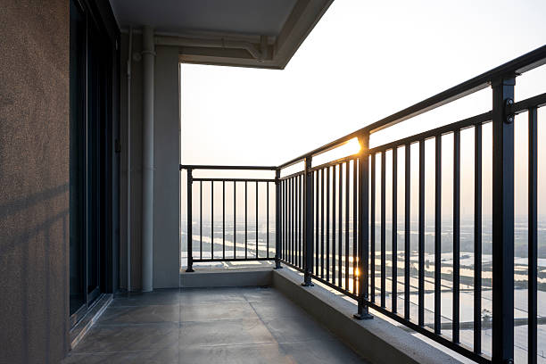 Modern urban balcony overlooking a city skyline during sunset, featuring metal railings and concrete flooring. The visual style is minimalist and contemporary, evoking a sense of tranquility and modern living. Potential usage includes real estate marketing, architectural design inspiration, or lifestyle photography.