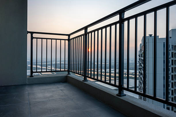 Modern urban balcony overlooking a city skyline during sunset, featuring metal railings and concrete flooring. The visual style is minimalist and contemporary, evoking a sense of tranquility and modern living. Potential usage includes real estate marketing, architectural design inspiration, or lifestyle photography.