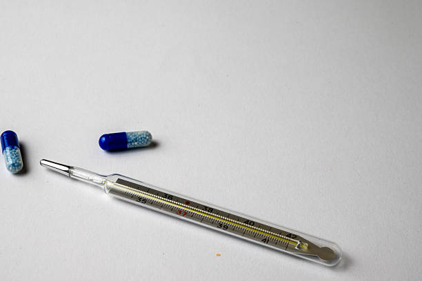 Top view of water soluble pills next to a glass thermometer showing fever symptoms