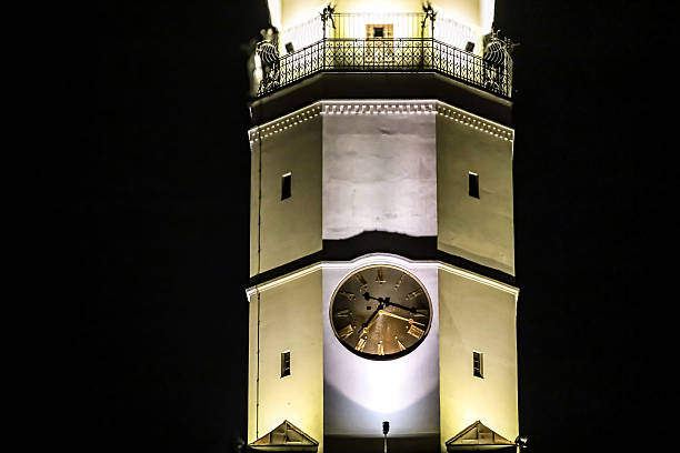 A detailed view of a historic clock tower illuminated by warm lights, showcasing its architectural features and a decorative railing at the top