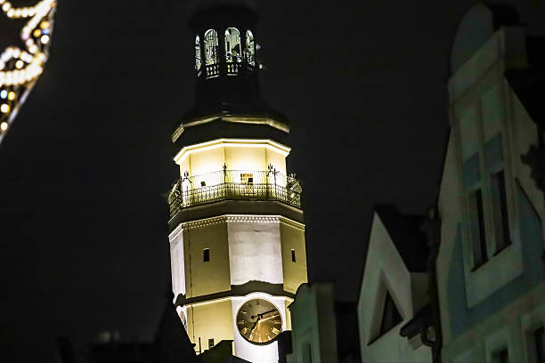 A detailed view of an old clock tower, lit up against the dark night sky, with decorative lights adding a festive atmosphere