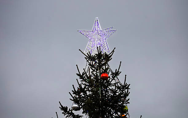 istock Illuminated star atop a decorated Christmas tree against a cloudy sky 2254094631