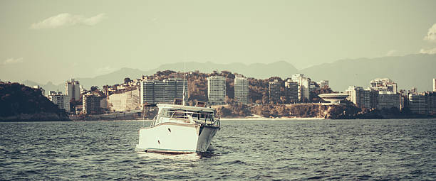 Telephoto view of a white motor yacht on calm sea with city skyline and distant mountains, selective focus and vintage tones, travel and luxury concept, copy space