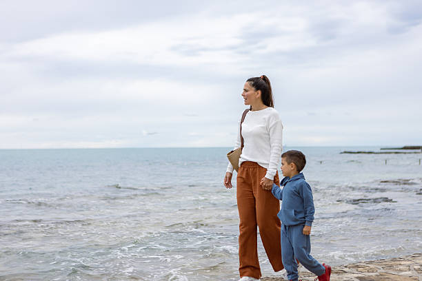 A serene photo capturing a mother and child holding hands while walking along the shoreline of a calm beach.