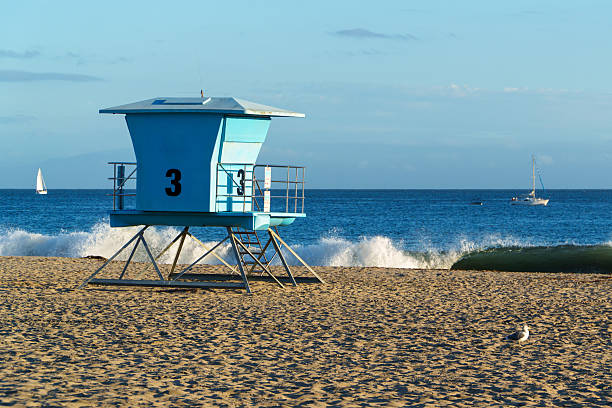 istock Light Blue Lifeguard Tower Number Three Standing Tall on a Sandy Beach with Crashing Waves and Sailboats on the Ocean Horizon 2254107176