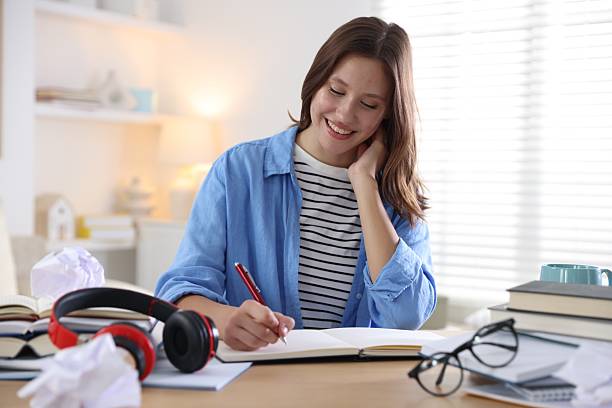 istock Smiling student with pen and books preparing for exam at table indoors 2254108335