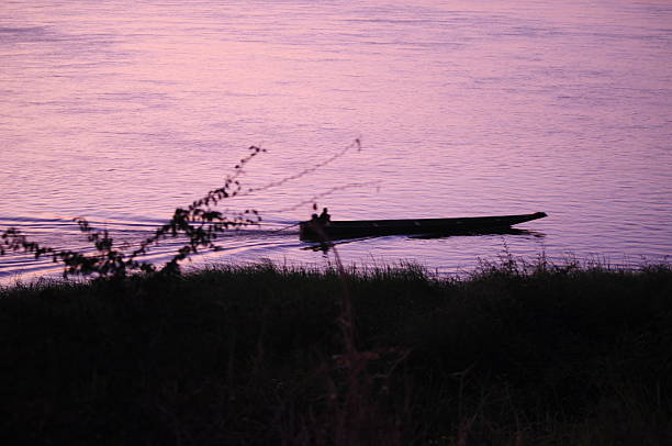 Embark on a journey of tranquility as you glide along the serene waters of Laos, aboard a traditional wooden boat. Against the backdrop of a radiant sunset, the sky is ablaze with hues of orange and gold, casting a warm glow over the tranquil landscape. From the vantage point of the boat, the scenery unfolds in a breathtaking panorama of misty mountains, lush foliage, and rippling water, creating a scene of timeless beauty and serenity. As the sun dips below the horizon, casting a shimmering reflection on the water's surface, a sense of peace and harmony envelops the surroundings, inviting contemplation and reflection. In this magical moment, immerse yourself in the beauty of nature and savor the tranquility of the sunset-drenched landscape unfolding before your eyes.
