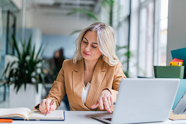 istock Businesswoman working in office space, writing notes while using laptop and focusing on tasks 2254112851