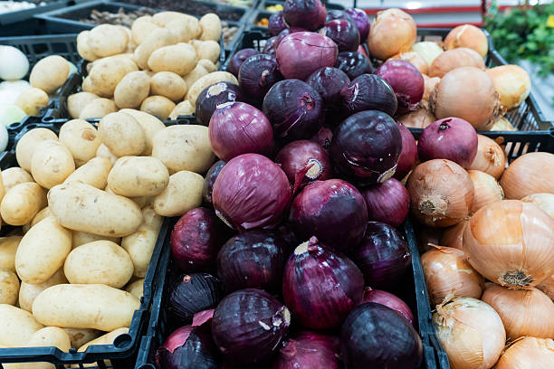Fresh potatoes, red onions and yellow onions in a black plastic container