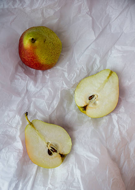 A whole pear and two pear halves are displayed on crinkled white paper