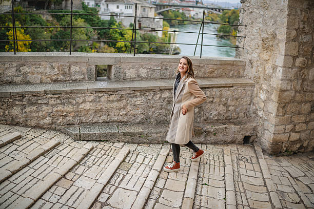 A young woman walks down the stone steps in Mostar, Bosnia and Herzegovina. She enjoys her time outdoors, taking in the view of the river and nearby buildings.
