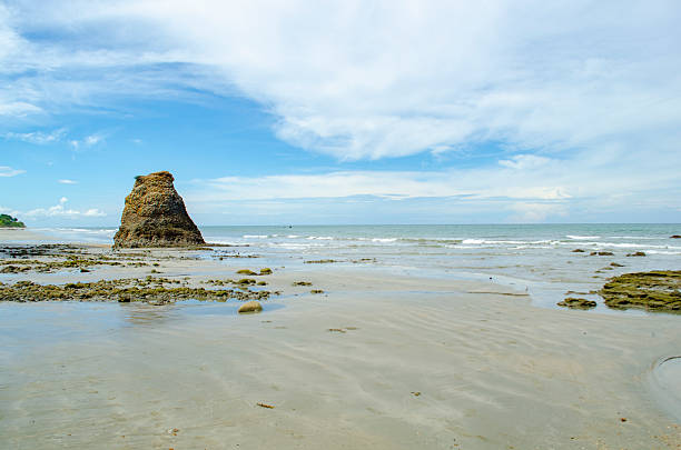 Low tide coastal view with a sea stack, shallow pools, and pale clouds stretching wide, Kuala Penyu, Sabah, Malaysia