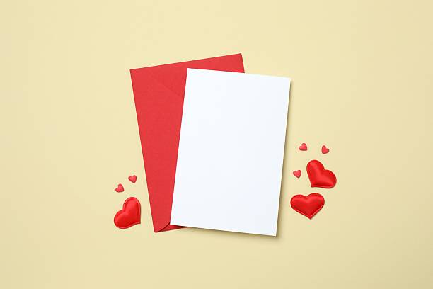 Red paper envelope with blank white note mockup inside and Valentines hearts on beige background. Flat lay, top view. Romantic love letter for Valentine's day concept.
