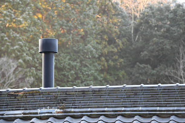 A wood-burning stove chimney stretching out from the tiled roof of a traditional Japanese house