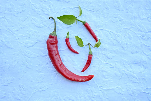 Organic red hot chili peppers with green leaves arranged on a blue fabric background. Minimalist culinary concept for healthy cooking.