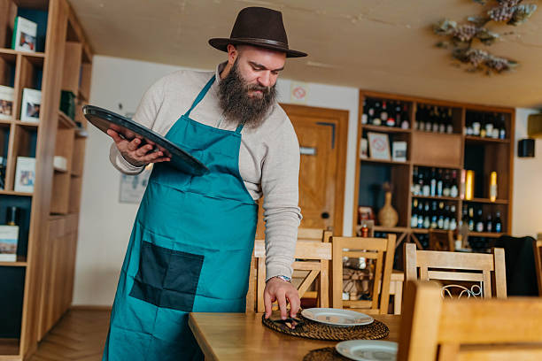 istock Smiling waiter cleaning and organizing tables 2254140694