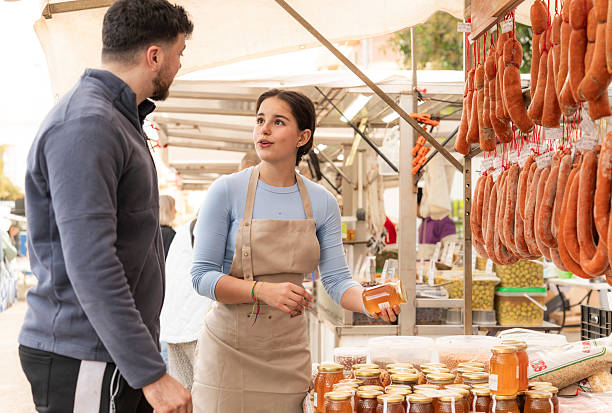 Vendor selling honey at market stall to customer