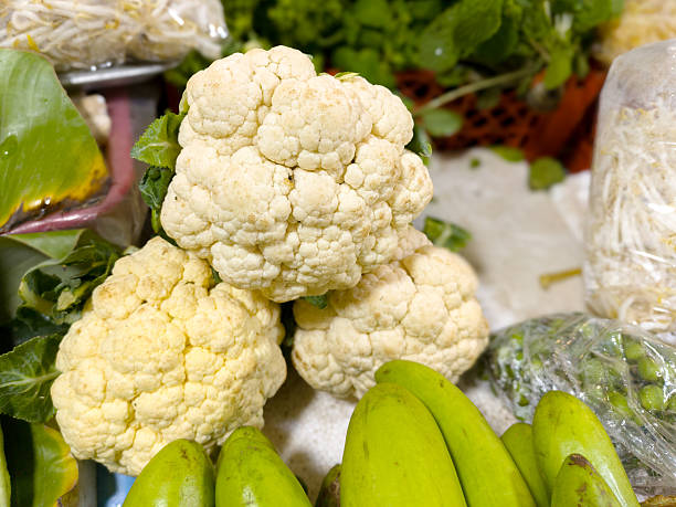 Close-up of fresh cauliflower and assorted vegetables displayed at market. Perfect for food, cooking, and healthy themes.