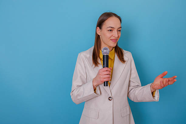 istock Confident young woman is giving a public speech into a microphone while making hand gestures against a backdrop of blue 2254149552