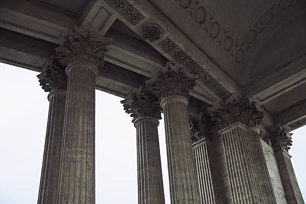 Stately colonnade featuring tall corinthian columns under detailed entablature, captured from low angle. Soft natural light highlights carved decorative elements against overcast sky