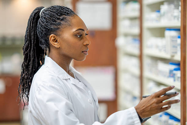 istock Black Woman Pharmacist In White Lab Coat Selecting Items On Pharmacy Shelf 2254153884