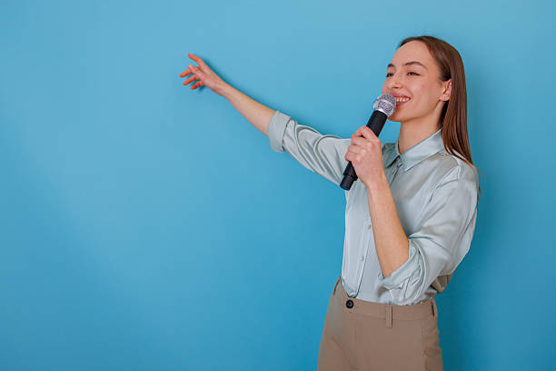 istock Woman holding microphone and pointing, giving a speech at a presentation or event. She is smiling and gesturing 2254157669