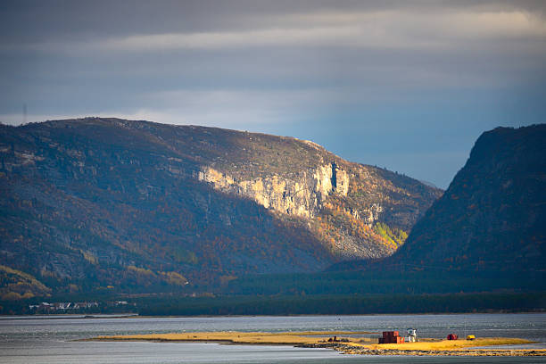 Scenery of mountains by the water in Talvik, Troms og Finnmark. The landscape shows a mix of rocky cliffs and gentle shores under a cloudy sky. This spot invites exploration and adventure.