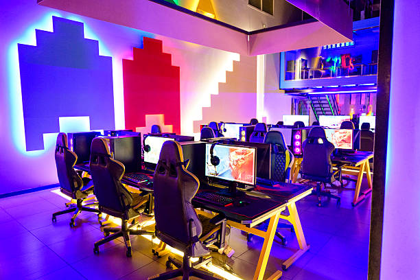 Empty e-sports gaming center featuring multiple computer stations with headphones, glowing keyboards, and vibrant  wall decorations creating a futuristic atmosphere