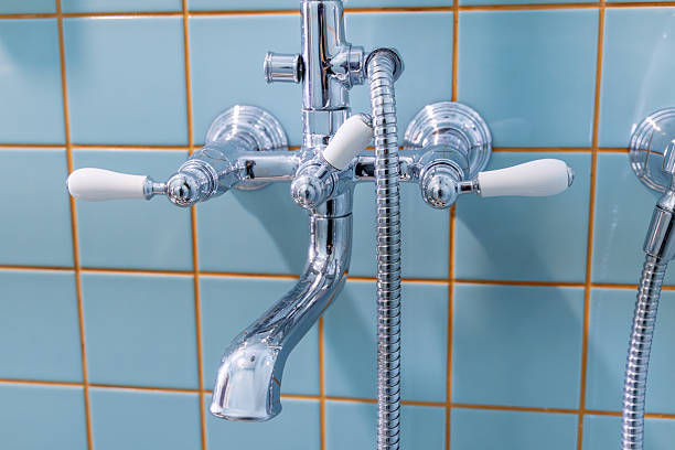 Chrome vintage faucet with white ceramic handles mounted on blue tiled wall in bathroom