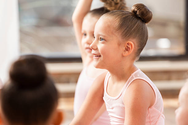 Children in ballet class, focused and engaged. Young dancers with hair in buns, smiling and listening to instructions.