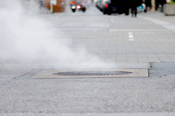 Damaged district heating pipeline in opened manhole, with steam and hot water spraying