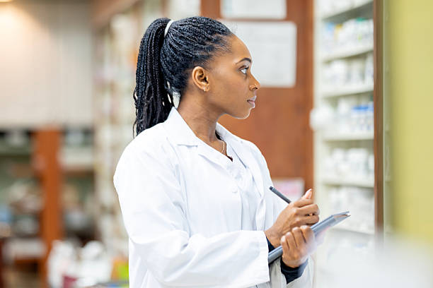 Black Female Scientist In White Lab Coat Analyzing Checklist At Pharmacy Or Lab